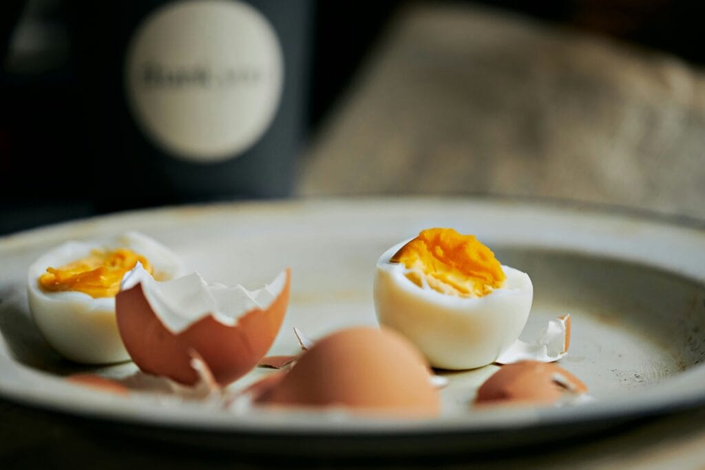 hard boiled egg peeled and halved on stoneware plate with shell pieces 