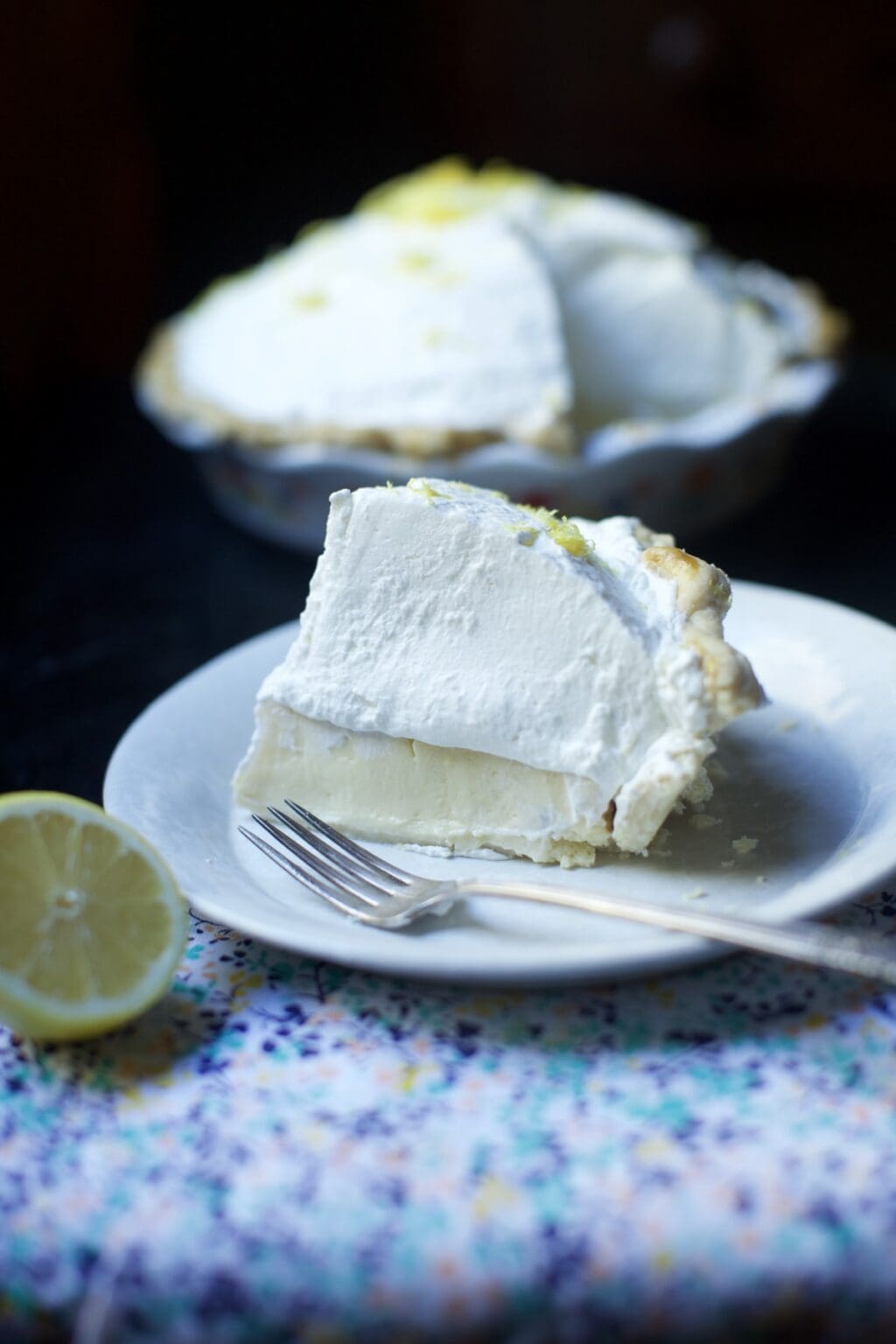 slice of tall, creamy lemon icebox pie on white plate with pie in background