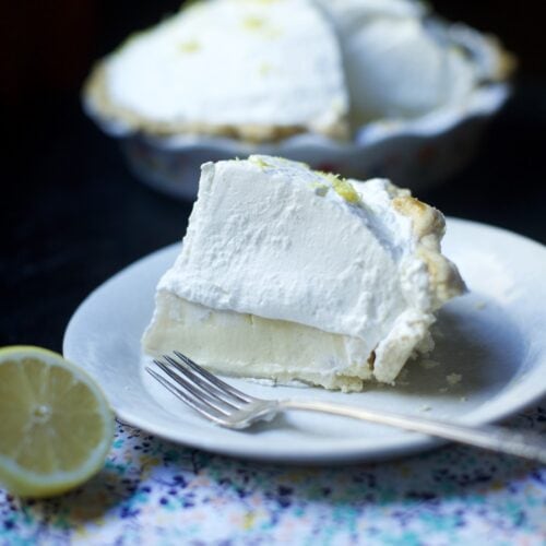 slice of tall, creamy lemon icebox pie on white plate with pie in background