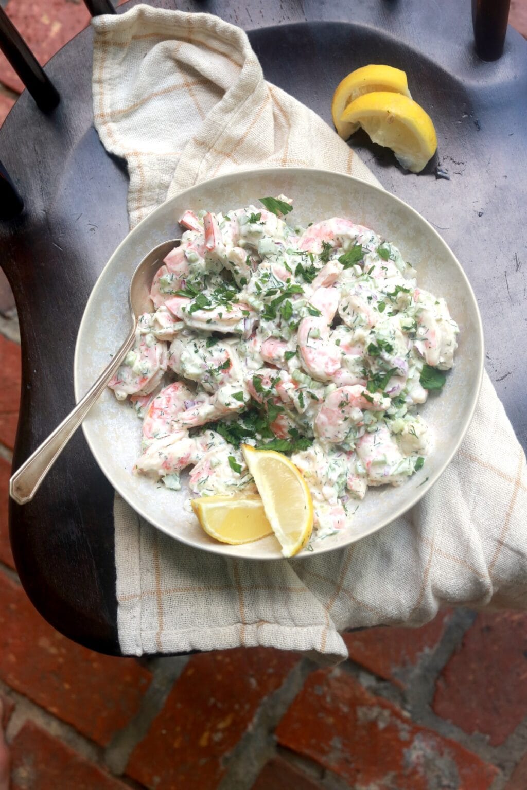 Delicious shrimp salad with herbs and lemon wedges on a white plate.