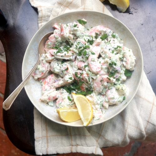 Delicious shrimp salad with herbs and lemon wedges on a white plate.