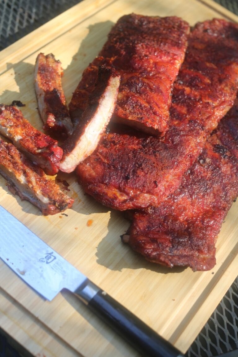 Juicy smoked ribs with a crispy bark on a wooden cutting board outside