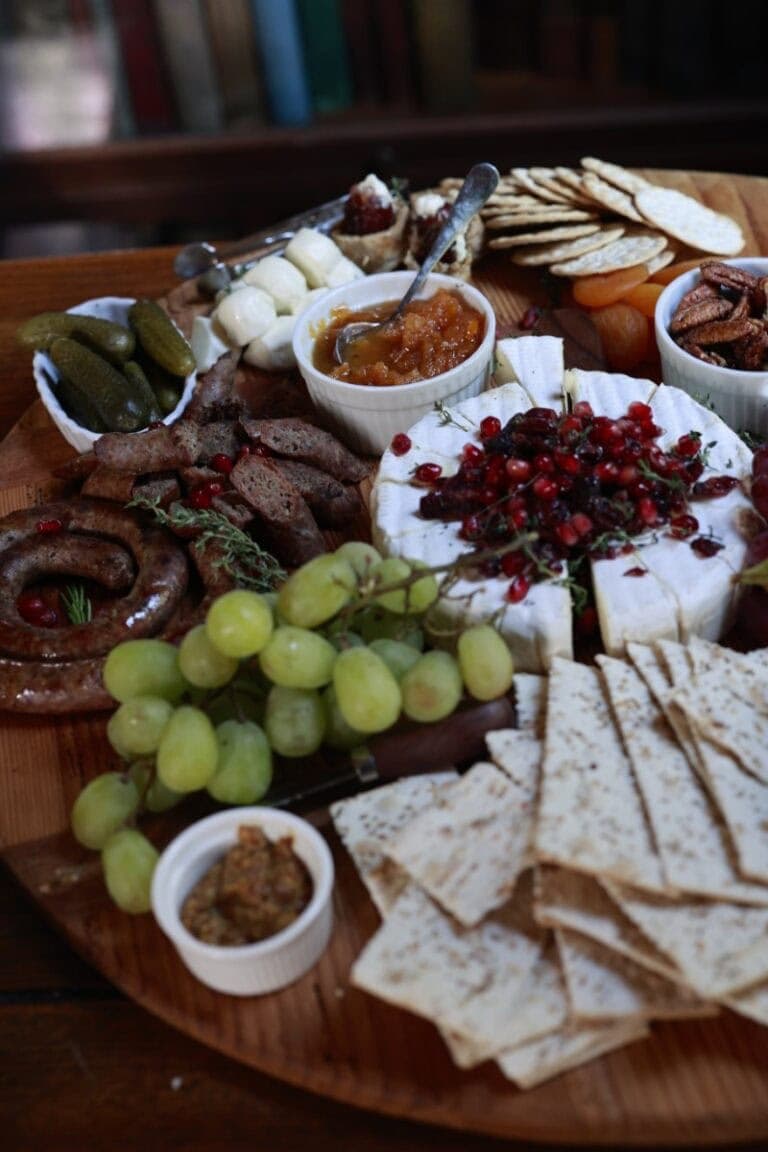 pork sausage, assorted cheese, fruits, and crackers on a wooden platter for snacking.
