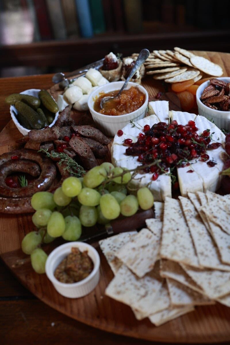 pork sausage, assorted cheese, fruits, and crackers on a wooden platter for snacking.